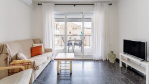 A living room with a sofa, a table, a TV, and a balcony with a view of buildings. - Apartment 'Mar 4 En Santa Pola' with Sea View, Private Terrace and Wi-Fi (Santa Pola)