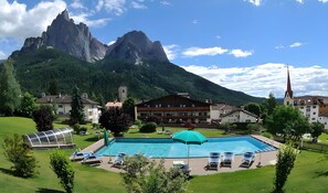 Et hotel med swimmingpool, liggestole og et bjerg i baggrunden.