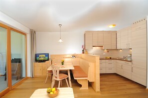 Une cuisine moderne avec des meubles en bois, un coin repas avec un banc et un téléviseur.