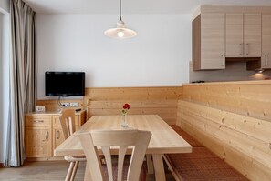 Una cocina moderna con armarios de madera, una mesa de comedor, sillas, un televisor y una lámpara colgante.