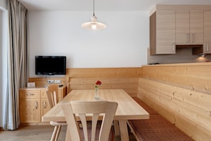 Une cuisine moderne avec des meubles en bois, une table à manger, des chaises, un téléviseur et un luminaire suspendu.