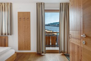Une chambre avec un lit, une armoire en bois et une vue sur un immeuble, visible à travers une fenêtre ornée de rideaux.