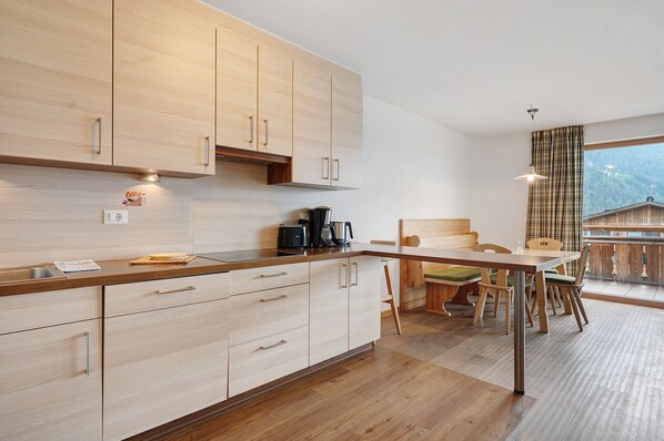 Une cuisine moderne avec des meubles en bois, un coin repas comprenant une table et des chaises, et une vue sur une montagne par la fenêtre.