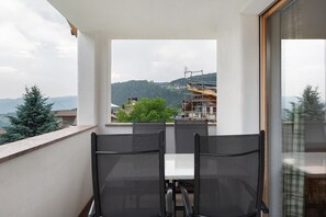 Un balcon avec une table et des chaises, une vue sur un paysage verdoyant et, au loin, un bâtiment en construction.