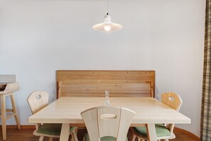 Un comedor con una mesa de madera, cuatro sillas, una lámpara colgante y un cabecero de madera.
