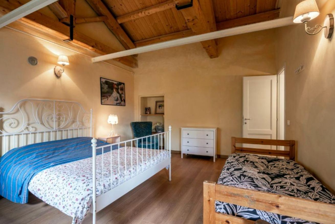 A bedroom with two beds, wooden ceiling beams, and a white door.