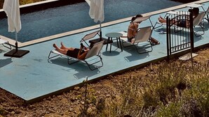 Ett poolområde med solstolar och parasoller, omgivet av en vacker utsikt över böljande kullar och vingårdar.