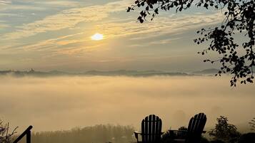 A sunrise over a foggy landscape with two Adirondack chairs facing a body of water.