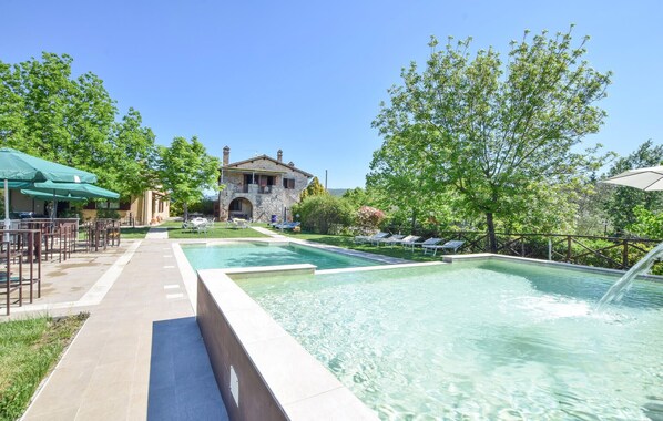 A pool area with lounge chairs, a stone building, and a clear sky.