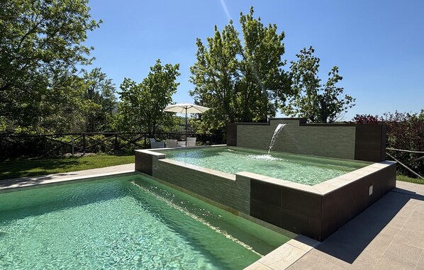 Une piscine rectangulaire agrémentée d’une cascade, entourée d’une clôture en bois et d’une végétation luxuriante.