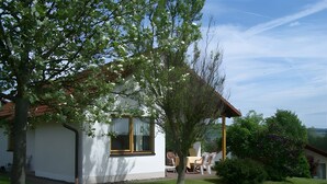 Una casa de fachada blanca, una ventana con marco amarillo y un patio con mobiliario exterior.