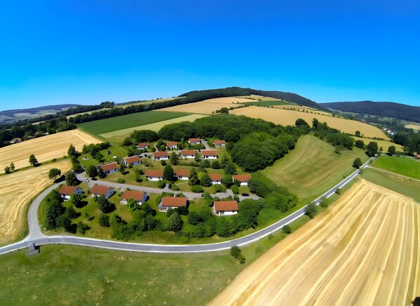 An aerial view of a rural area with a cluster of houses, a winding road, and surrounding fields.