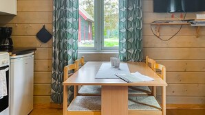 Una mesa de madera para comer con cuatro sillas, una cafetera y una ventana con cortinas.