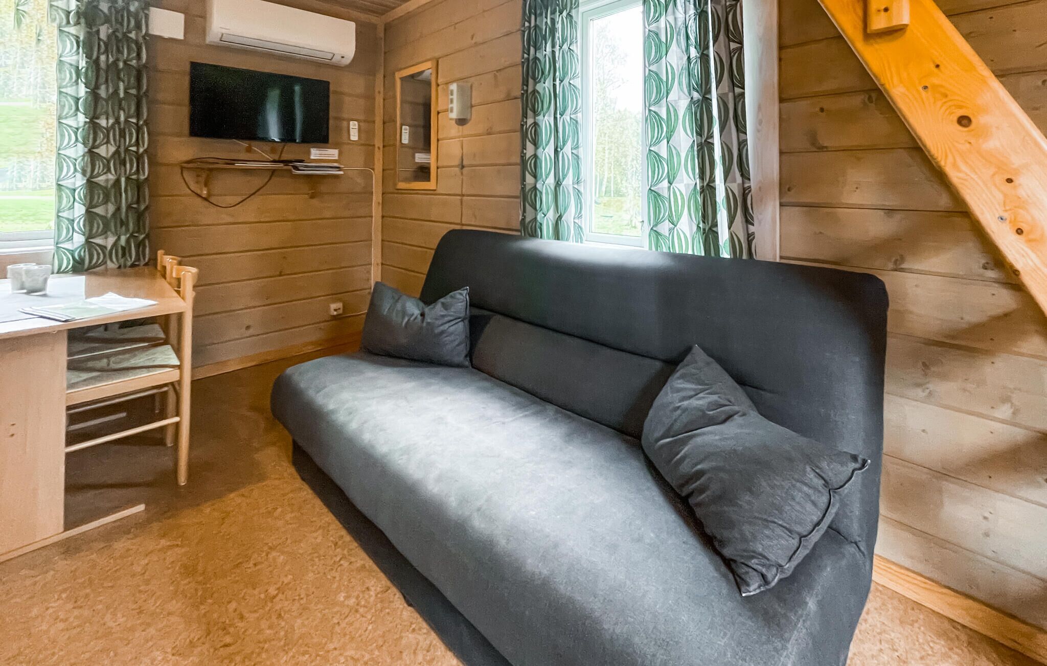 Een houten kamer met een grijze bank, een klein bureau en een televisie aan de muur.