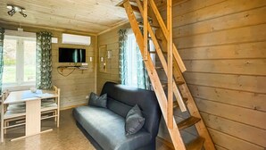 A cozy room with a wooden floor, a sofa, a desk with a chair, a TV mounted on the wall, and a wooden ladder leaning against the wall. - 1 bedroom gorgeous home in Våxtorp (Våxtorp)