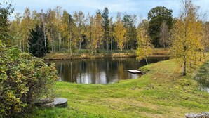 Un entorno tranquilo junto al lago, con un muelle de madera que se adentra en el agua, rodeado de exuberante vegetación y árboles con tonos otoñales.