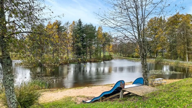 Un parque junto al lago con un muelle de madera y un tobogán azul.