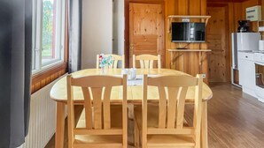 Una mesa de comedor de madera con cuatro sillas, un televisor montado en la pared y una cocina con electrodomésticos.