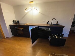 A compact kitchen with a built-in oven, a sink, and a countertop with a coffee maker.