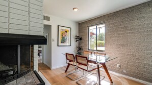 Ein modernes Interieur mit Kamin, Essbereich mit Glastisch und Korbstühlen sowie einer Ziegelwand.