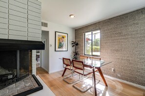 A modern interior with a fireplace, a dining area with glass-top table and wicker chairs, and a brick wall. - 1 Mi to Dtwn & Mill Avenue! Home w/ Outdoor Oasis (Tempe)
