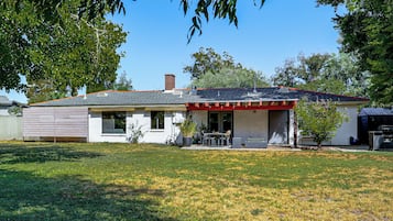 Een gelijkvloers huis met een overdekt terras, schoorsteen en gazon.