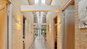 Un pasillo con paredes de ladrillo y vigas de madera, que conduce a una habitación con un ventanal y una puerta.