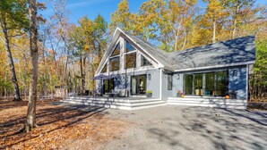 A modern house with a large porch, surrounded by trees and a gravel driveway. - 'Valhalla': Family Home on Frye Island w/ Golf! (Frye Island)