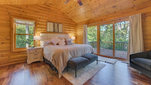 A wooden cabin bedroom with a bed, bench, nightstand, and a view of the outdoors. - Luxury Cabin in The Reserve at Boyne Mountain (Boyne City)