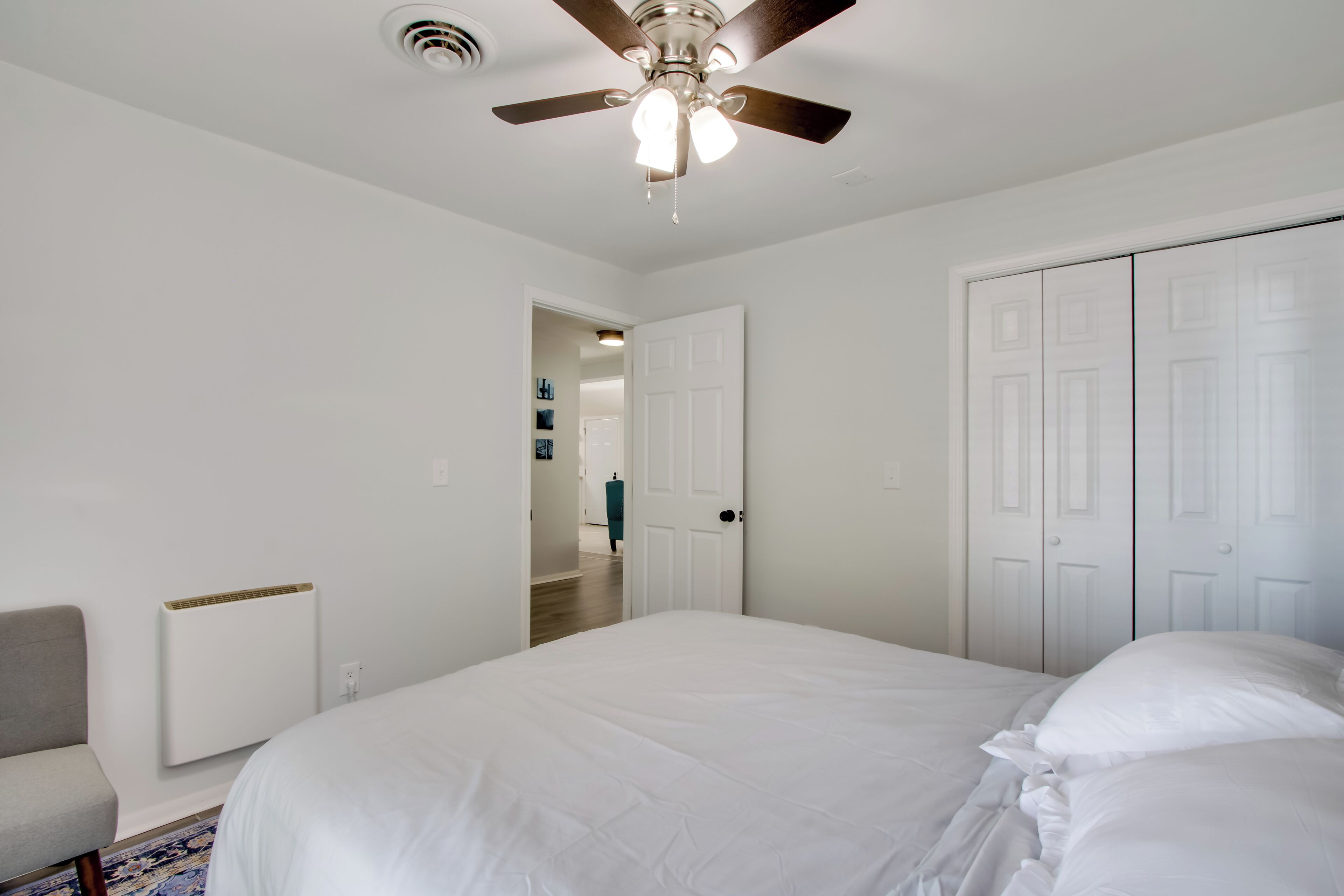 Une chambre à coucher comprenant un lit, un ventilateur de plafond, un radiateur, une chaise et une armoire.