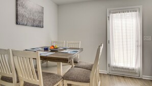 Un comedor con una mesa de madera, seis sillas, un cuenco de fruta y un cuadro en la pared.