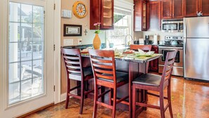A kitchen with wooden cabinets, a stainless steel refrigerator, and a dining area with a table and chairs. - Heart of Historic Chickamauga! Chic Studio w/ Pool (Chickamauga)