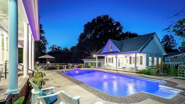 A swimming pool with lounge chairs, a covered patio, and a building with a gabled roof. - Heart of Historic Chickamauga! Chic Studio w/ Pool (Chickamauga)