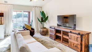 Ein Wohnzimmer mit einem weißen Sofa, einer Holz-Unterhaltungsecke, einer großen Pflanze und einem Fernseher.