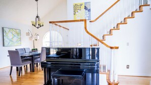 Un vaste salon agrémenté d’un magnifique piano à queue, d’un escalier en bois et d’un coin repas avec des chaises et une table.