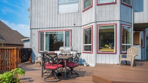Une terrasse avec un barbecue et du mobilier d’extérieur, une clôture en bois et une maison dotée de grandes fenêtres et d’une porte.