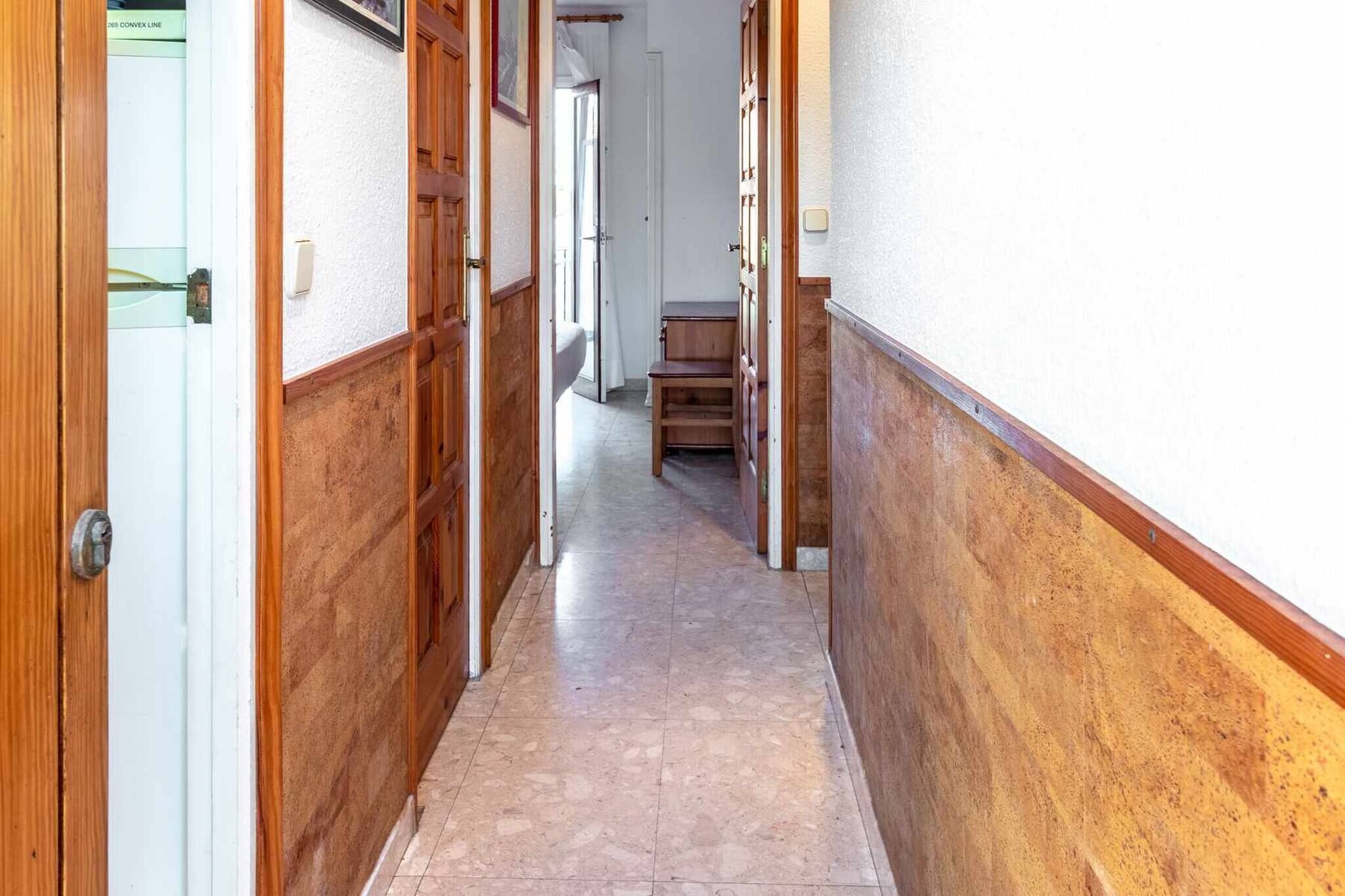 Un couloir étroit avec des portes en bois et un sol carrelé.