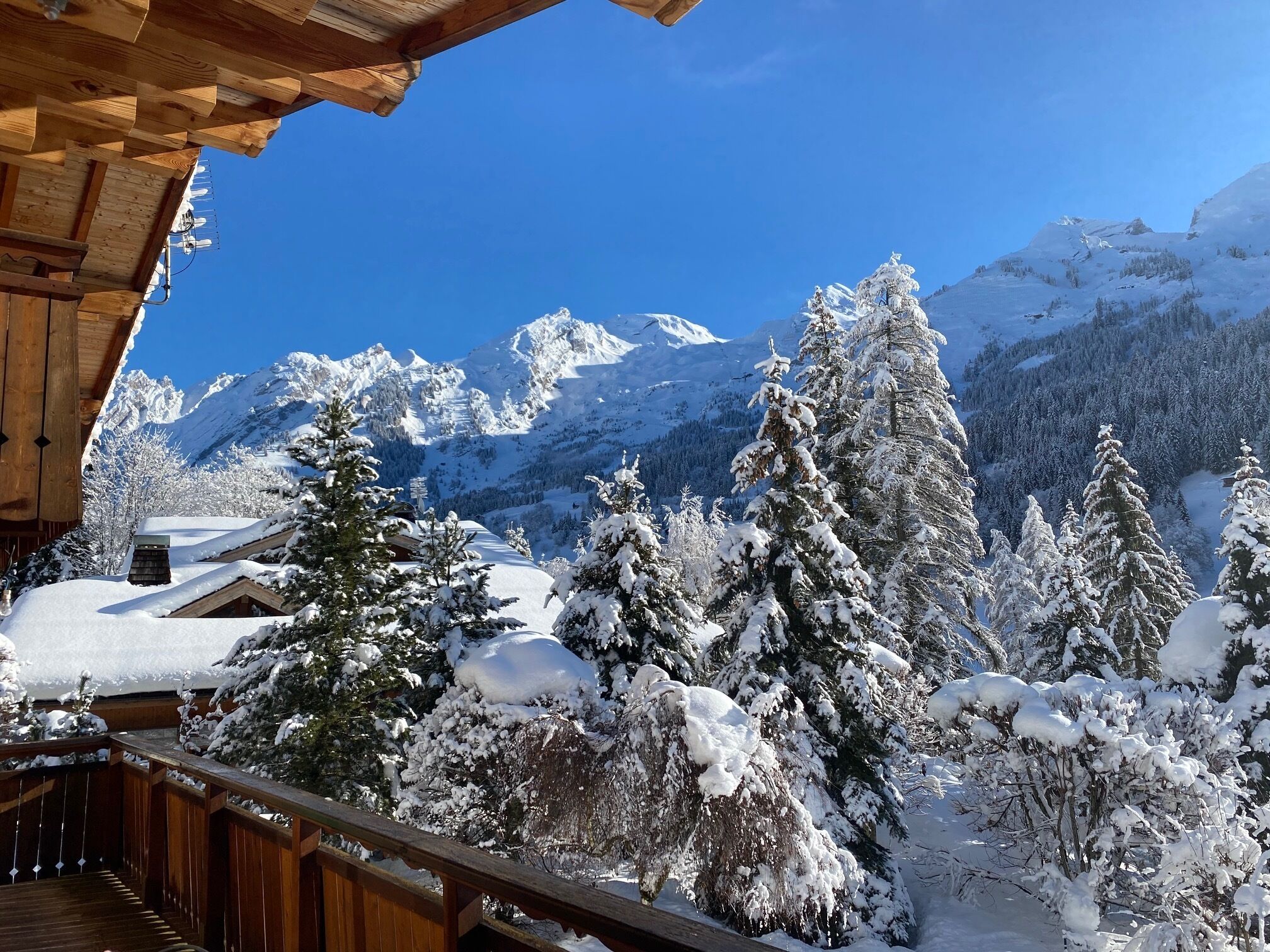 A wooden deck overlooking a snowy mountain landscape with a clear blue sky.