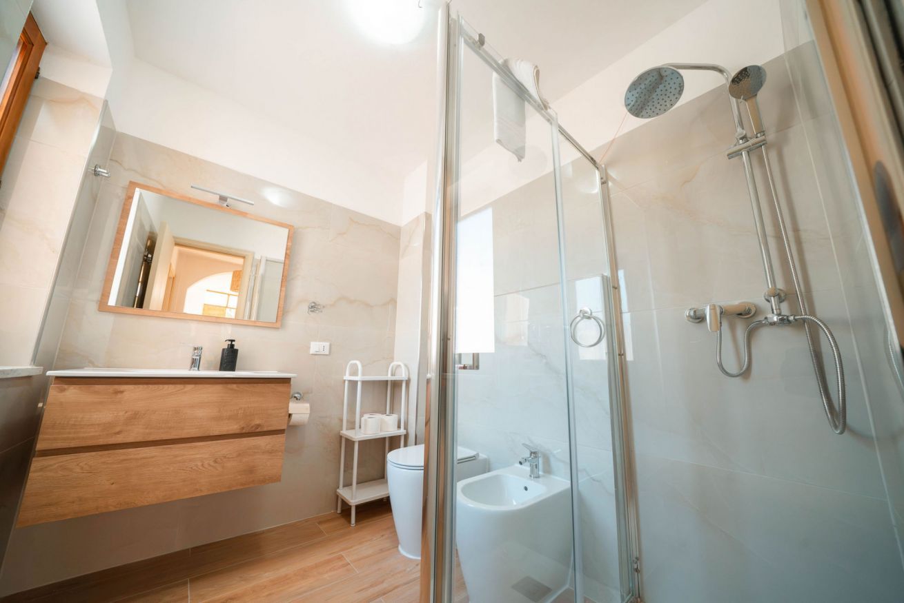 Ein modernes Badezimmer mit Duschkabine aus Glas, einem Holzwaschtisch und einer Wand mit Marmorfliesen.
