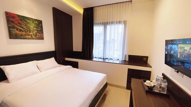 A hotel room with a large bed, a desk with a TV, a window with curtains, and a painting on the wall. - UMASAN COLIVING & RESTO PONDOK INDAH (Jakarta)