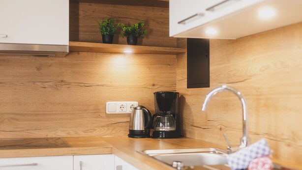 A kitchen with wooden cabinets, a stainless steel sink, a coffee maker, and two potted plants on a shelf. - Apartment 16 – Haus Voglreiter with Mountain View, Shared Garden and Wi-Fi (Kaprun)