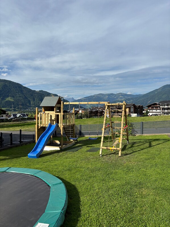 A playground with a slide and swings, surrounded by a grassy area and buildings in the background.