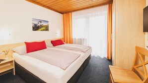 A hotel room with two beds, a wooden ceiling, a TV, and a window with curtains. - Apartment 16 – Haus Voglreiter with Mountain View, Shared Garden and Wi-Fi (Kaprun)