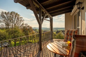 Un balcon avec une table et des chaises en bois, une vue sur la campagne et une balustrade.