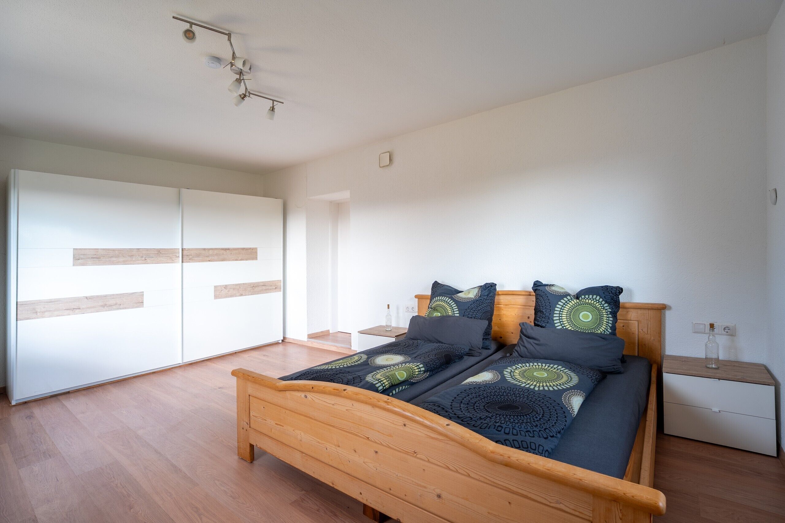 A bedroom with a wooden bed, a nightstand, a wardrobe, and a ceiling light fixture.