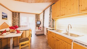 Eine kleine Küche mit Holzschränken, einem Esstisch mit Stühlen und einem Fernseher.