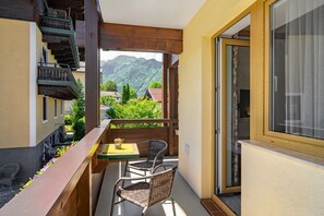 Un balcon avec des fauteuils en osier, une table avec un plateau en verre et une vue sur les montagnes.