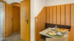 Ein Zimmer mit Holzwandverkleidung, einem Esstisch mit grüner Platzauflage und einer Schüssel mit Brot und Käse.