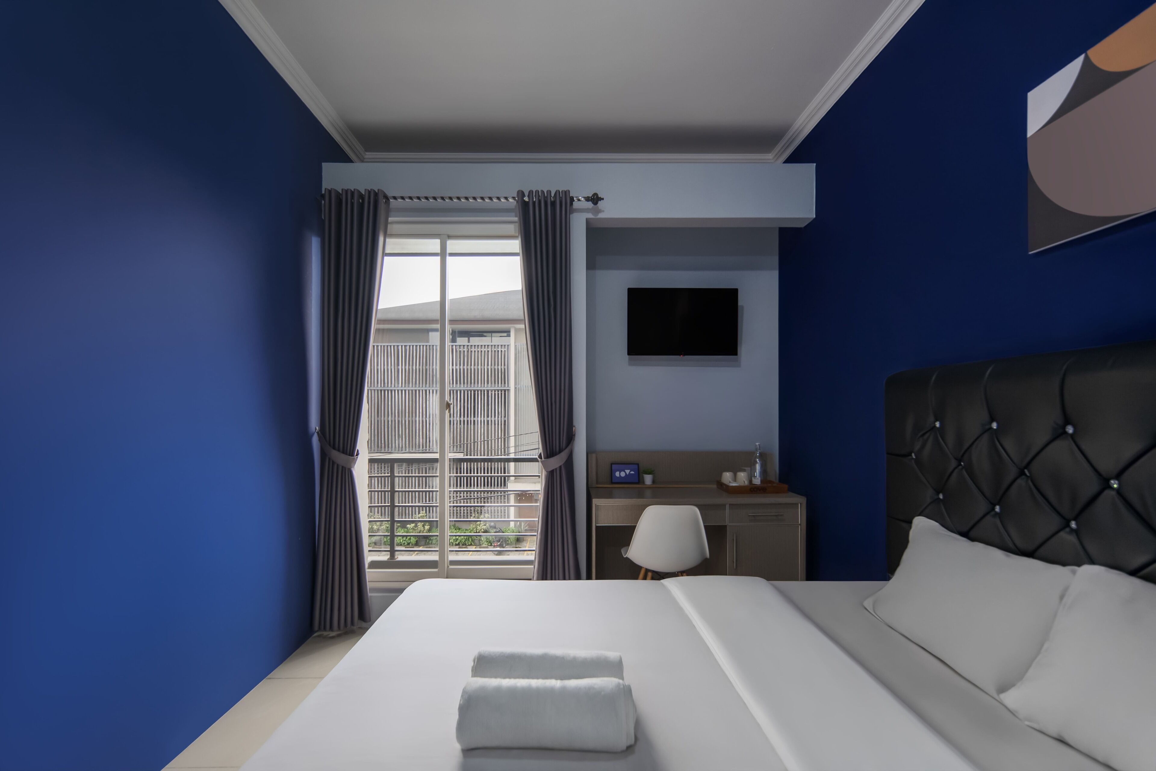 A hotel room with a bed, a desk, a chair, a TV, and a window with curtains.
