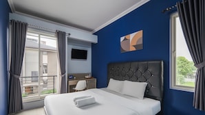 Una camera d'albergo con un letto, una scrivania, una sedia, una televisione e un balcone.
